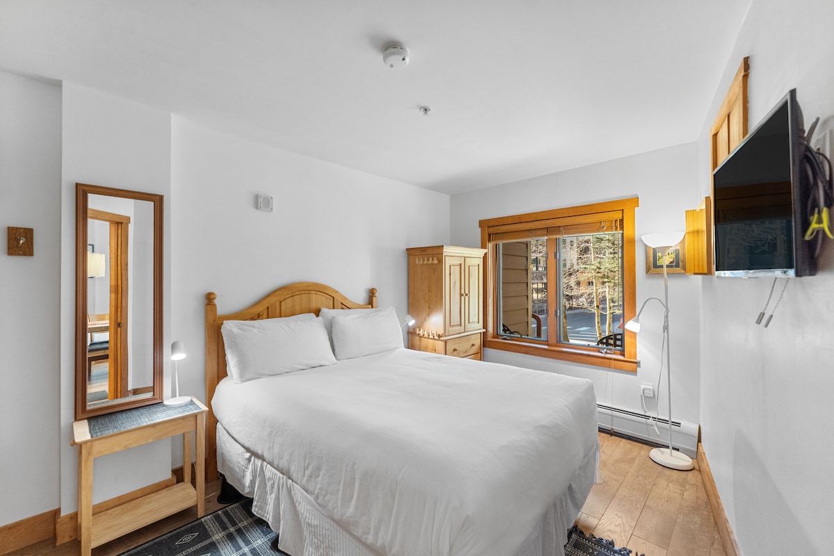 Chumba cha kulala kina kitanda cha ukubwa wa malkia pamoja na vitanda vyeupe na runinga ya skrini bapa.