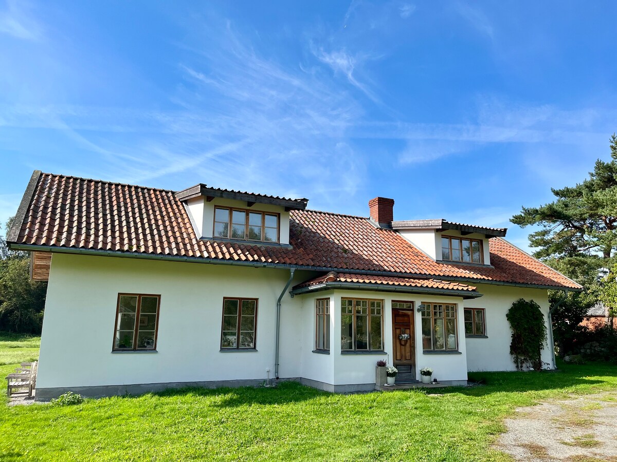 A spacious two-story house is set against a clear blue sky. A welcoming entrance door is flanked by large windows, allowing natural light to flood the interior. The well-maintained exterior features a red-tiled roof and green grass surrounding the structure.