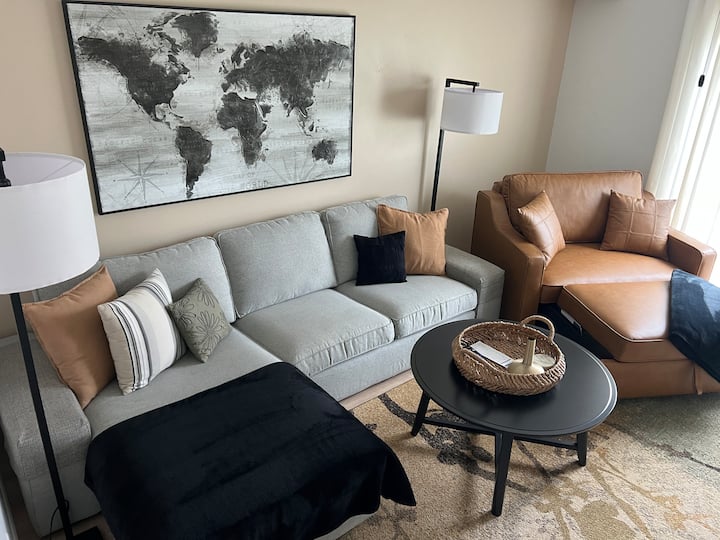 Living room w/smart TV, 2 lamps, coffee table, oversized sleeper chair & sofa with lounger. Office space in the corner. Access through the sliding door to ground level outdoor patio with fire pit and four Adirondack chairs.