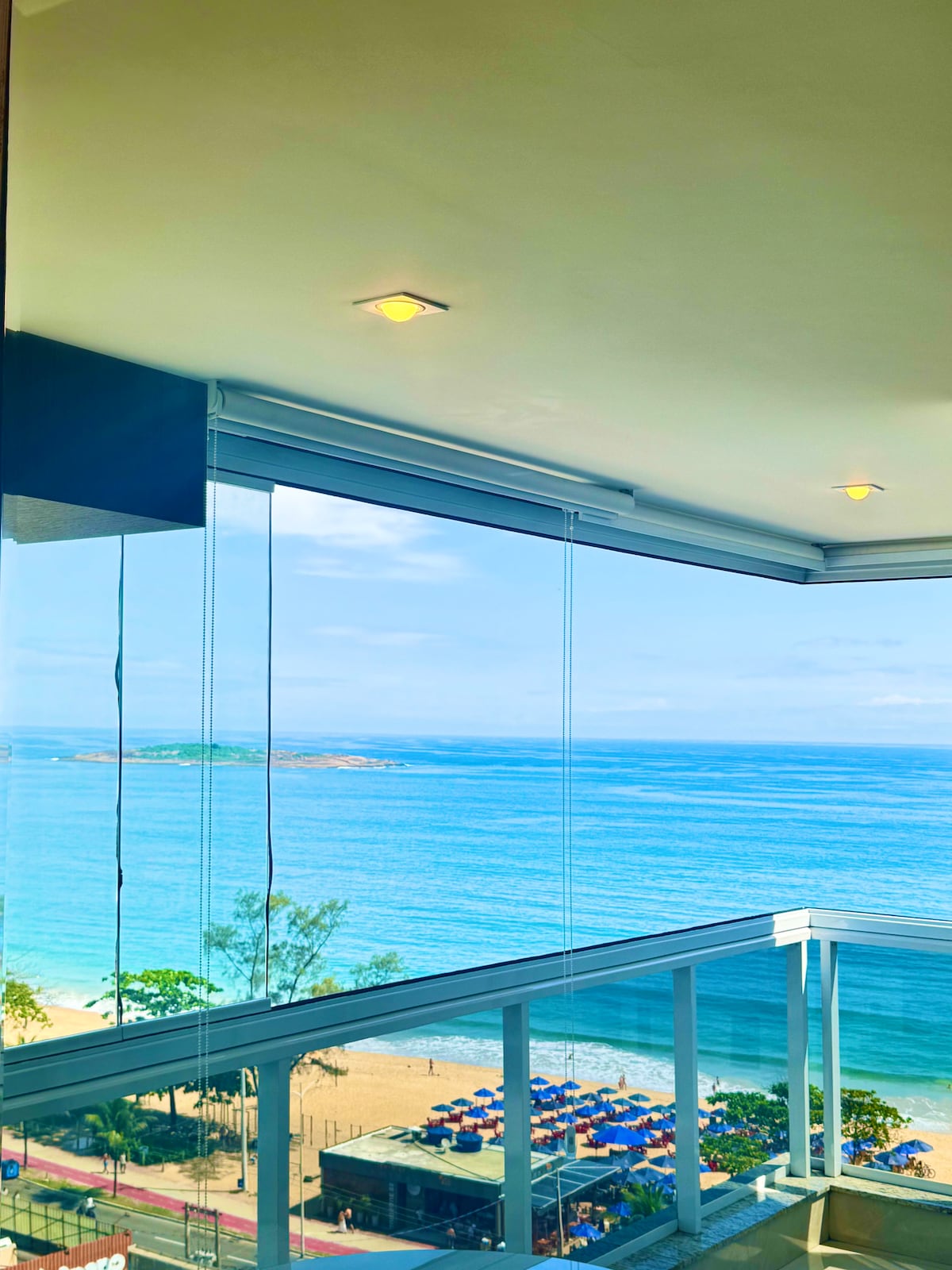 A bright and airy balcony offers expansive views of the tranquil ocean and clear blue sky. The glass walls create an open atmosphere, inviting natural light into the space. The coastal scenery enhances the backdrop, providing a serene setting for relaxation.