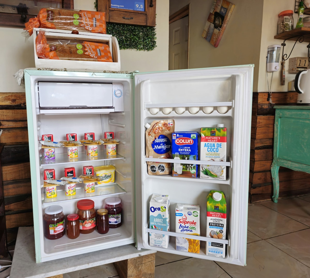 An open refrigerator displays an organized selection of food items. Shelves contain jars of jams, assorted yogurts, beverages, and various dairy products. The refrigerator's interior is well-lit, providing a clear view of the contents. Some items are stored in clear containers for easy identification.