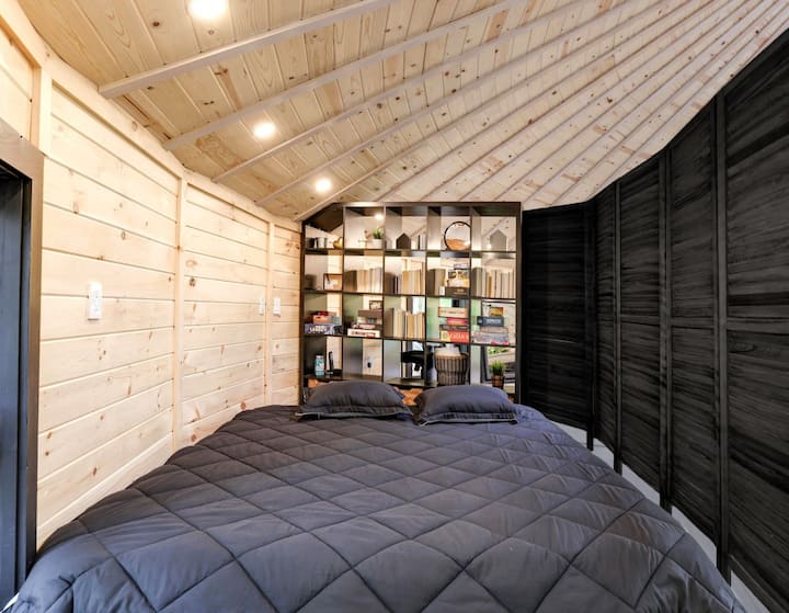 The loft bedroom tucks beneath the yurt's sloped wooden ceiling, with a bookshelf of reads and board games serving as a headboard.