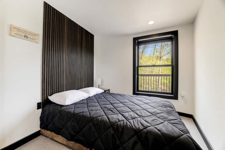 A restful bedroom with a slatted wood accent wall behind the bed and a window framing the surrounding trees.