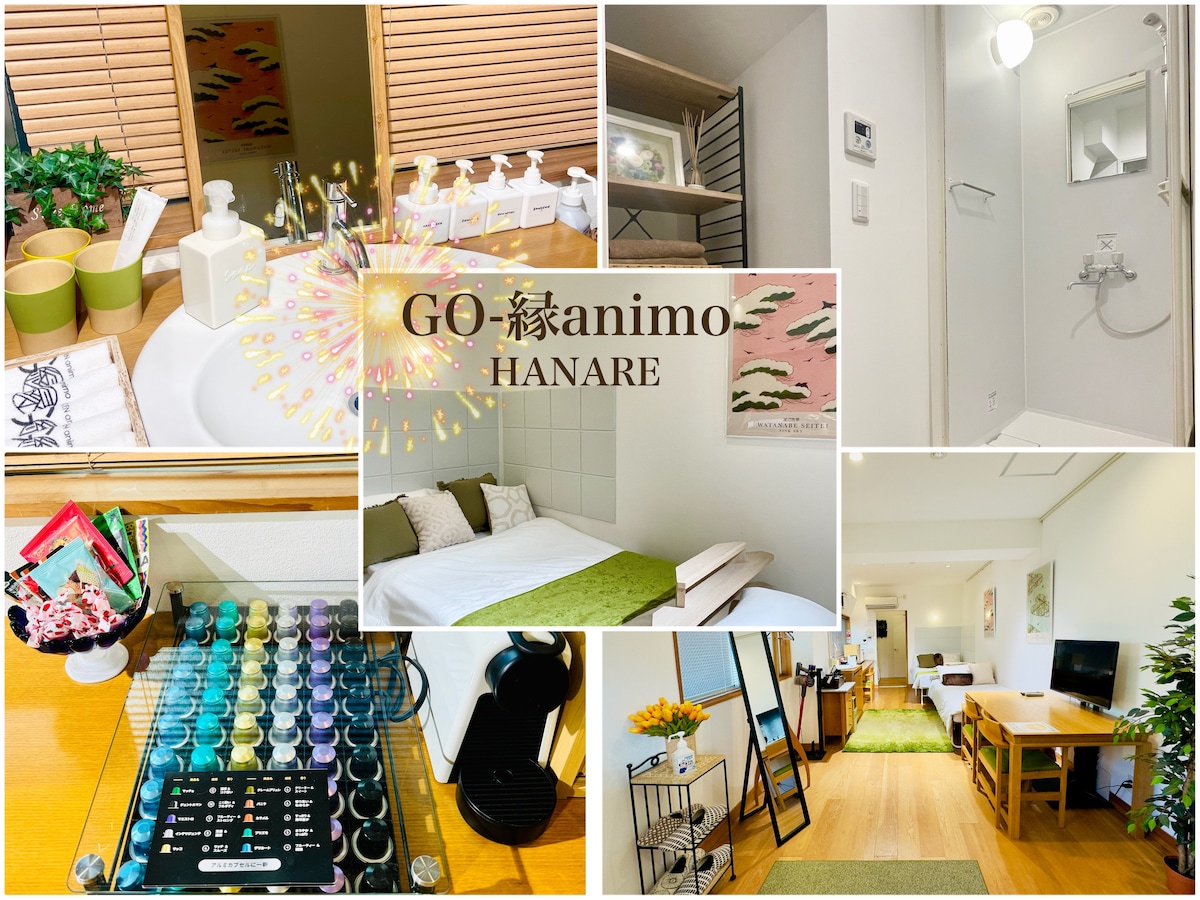 A modern, well-appointed space includes a cozy sleeping area with a spacious bed dressed in white linens. The kitchenette features utensils, and a shower area is visible. Natural elements like greenery enhance the welcoming environment, promoting comfort and ease for guests.