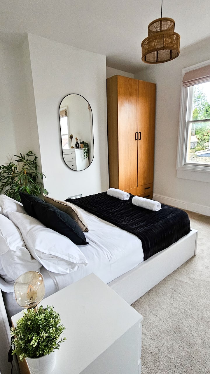 غرفة نوم مزدوجة مع مرتبة سيمبا هايبرد® مريحة وطاولات بجانب السرير وصندوق أدراج وخزانة ملابس وطاولة/مكتب تزيين.