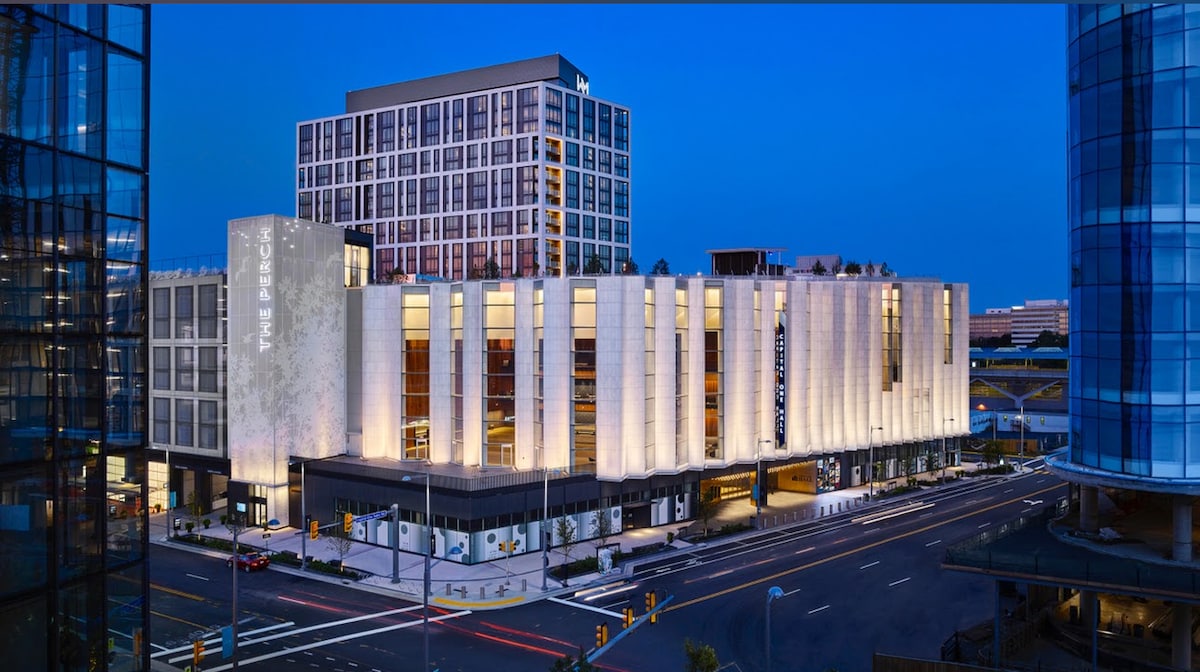 The modern building is showcased prominently at dusk, featuring a well-lit facade and large windows. The sleek architectural design is complemented by surrounding streets and urban landscaping, highlighting the contemporary setting in McLean, near the metro station.