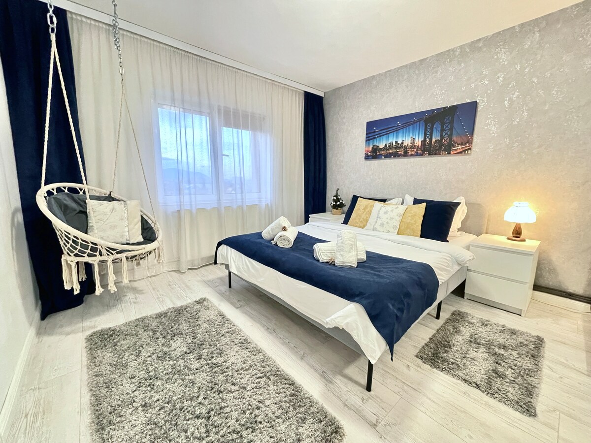 Moderno dormitorio equipado con una cama tamaño queen con sábanas de algodón, toallas mullidas, almohadas acogedoras, un enorme armario, calefacción, mesitas de noche, televisor inteligente y un elegante columpio para relajarse y cortinas opacas para un sueño profundo.