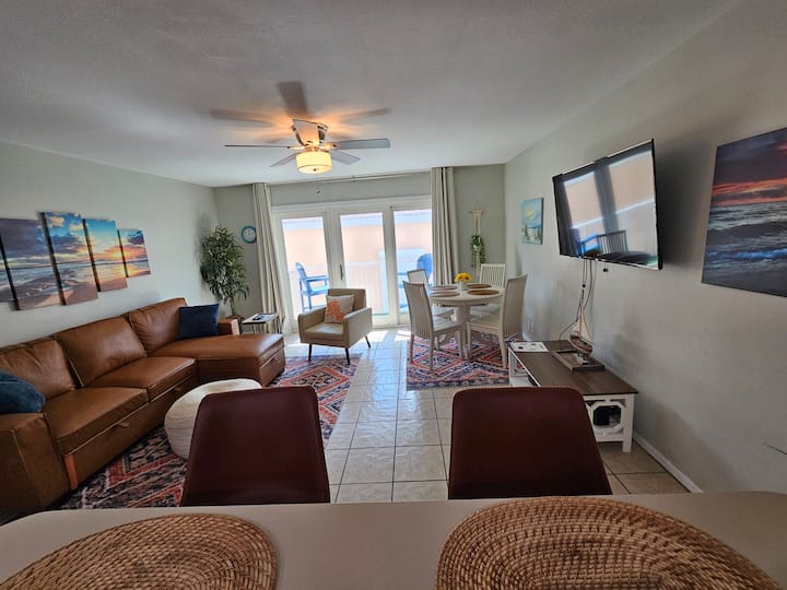 Bright, open-concept living room with a cozy leather sectional, smart TV, and stylish décor, perfect for relaxing after a beach day or hosting movie nights.