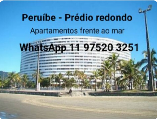 The image showcases a round building located along the beachfront in Peruíbe. Palm trees line the sandy shore in the foreground, while the building features multiple levels. The clear blue sky complements the seaside view, indicating a coastal atmosphere.