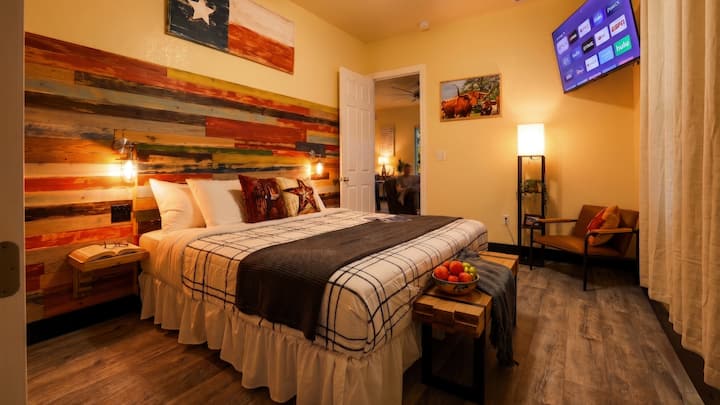 Experience true Texas comfort in this king bedroom, featuring a rustic wood accent wall, cozy seating, and a smart TV. Perfect for unwinding after a day of adventure, enjoy unique decor and modern amenities.