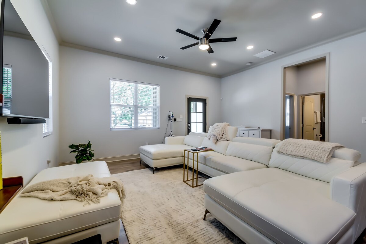 A spacious living area features a large sectional sofa and a cozy throw draped casually across the arm. Natural light enters through multiple windows, illuminating the room. A small coffee table sits near the sofa, enhancing the inviting atmosphere.