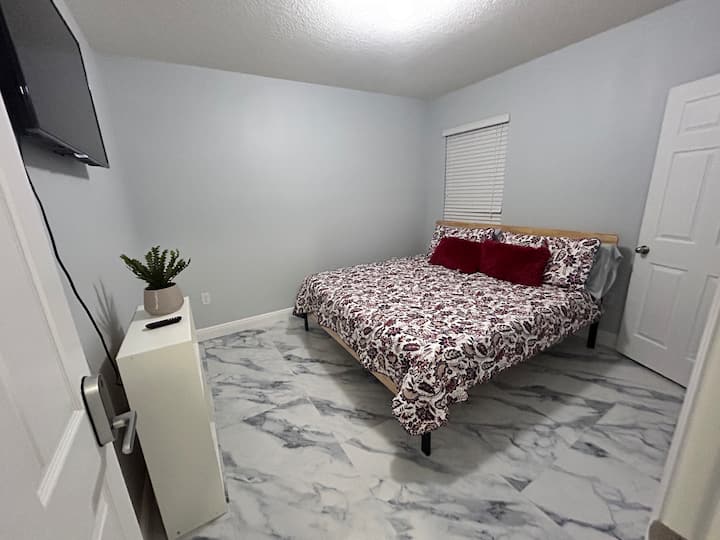 Chumba cha pili cha kulala kilicho na kitanda cha kifahari chenye matandiko na mito ya kifahari. Televisheni mahiri iliyowekwa kwenye ukuta, sakafu ya marumaru ya kifahari na kijani cha asili huunda sehemu tulivu ya wageni. Samani za kisasa na kuta laini za kijivu huhakikisha usingizi wa utulivu.