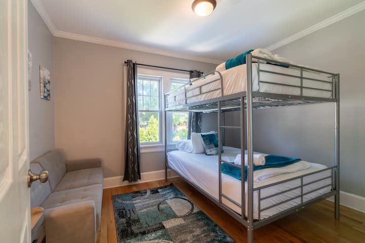 This remarkable suite features a sleek, modern bunk bed setup paired with a plush gray tufted sofa. Complete with premium linens, vibrant teal accents, and rich hardwood floors.