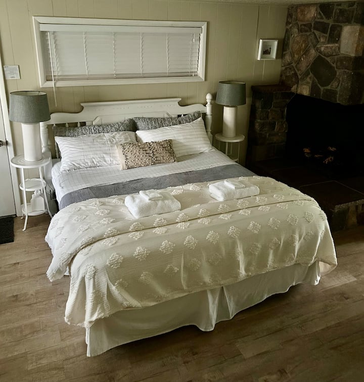 Cama tamaño king, chimenea adyacente y sofá cama. Espacio de apartamento tipo estudio con cocina pequeña.