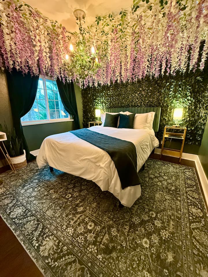 Welcome to your whimsical bedroom with hanging wisteria & twinkly lights! This bedroom has a queen bed, a desk for that remote worker, & a closet filled with extra amenities including an iron and ironing board, pack n play, board games & yoga mats. 