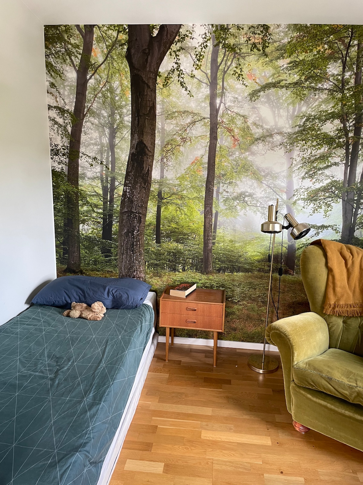 Spavaća soba s umirujućim šumskim tapetama, stolicom za čitanje i mogućnošću dodatnog madraca. 