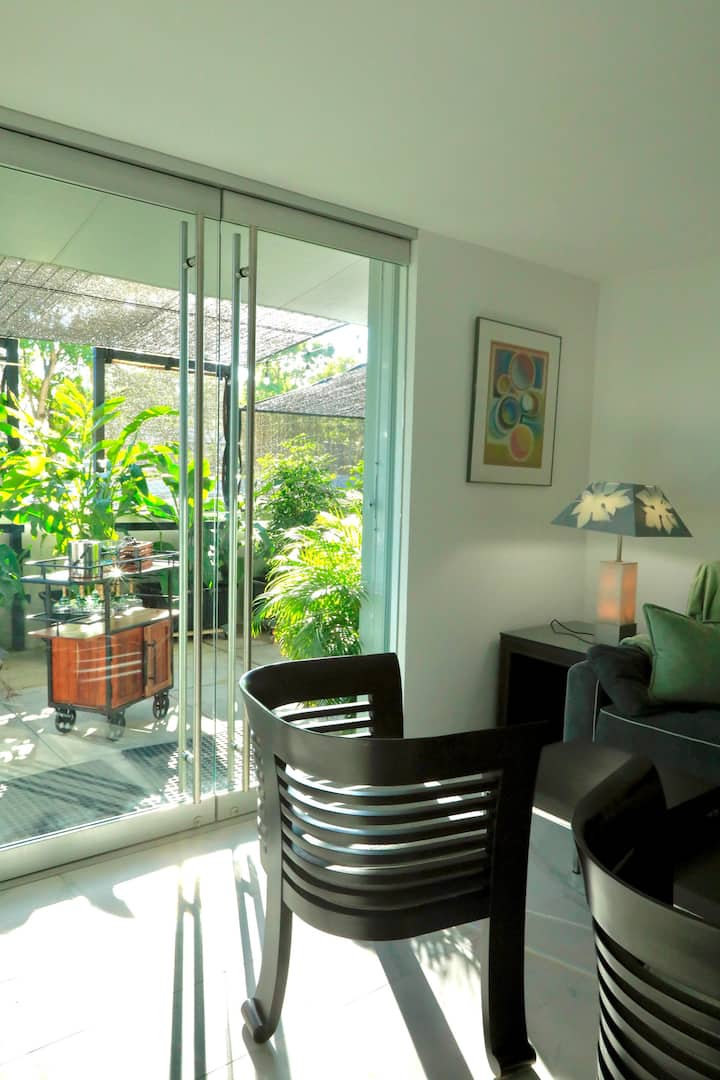 Milango ya kioo iliyo wazi kwenye mtaro wako binafsi, iliyojaa mimea ya kitropiki na baa ndogo inayoweza kubebeka inaweza kutumika ndani au nje.