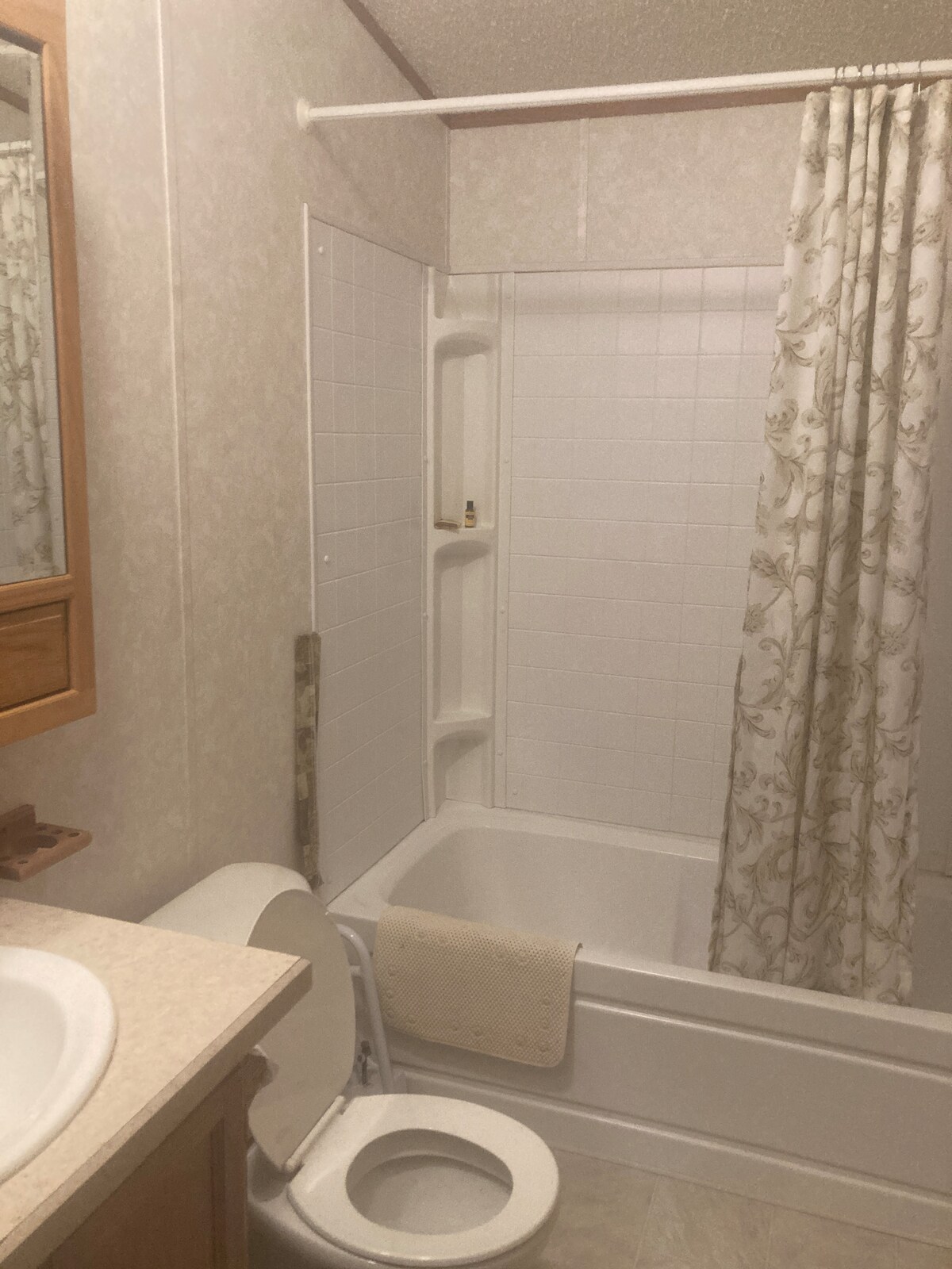 A compact bathroom features a standard bathtub with a shower curtain adorned with a floral pattern. A wooden vanity with a sink is positioned next to the bathtub. The space includes light-colored walls and light flooring, enhancing the overall brightness.
