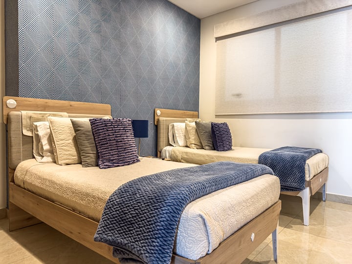 Dhomë dytësore me dy krevate tek, dekorim modern në nuanca blu, dollap i madh, televizor dhe ajër i kondicionuar.