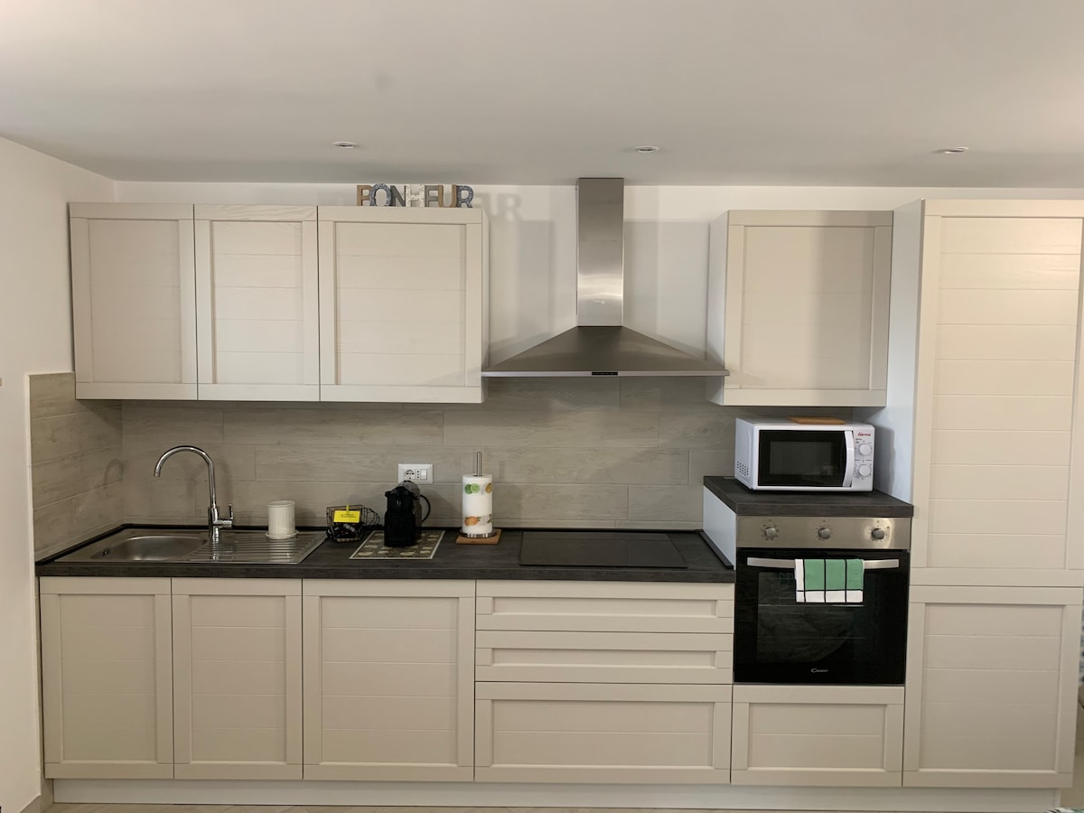 A modern kitchen showcases sleek cabinetry and a range of appliances, including a microwave and an oven. A stainless steel sink is positioned under the cabinetry. Counter space is available, complemented by neutral-toned surfaces and a decorative accent on top of the cabinets.