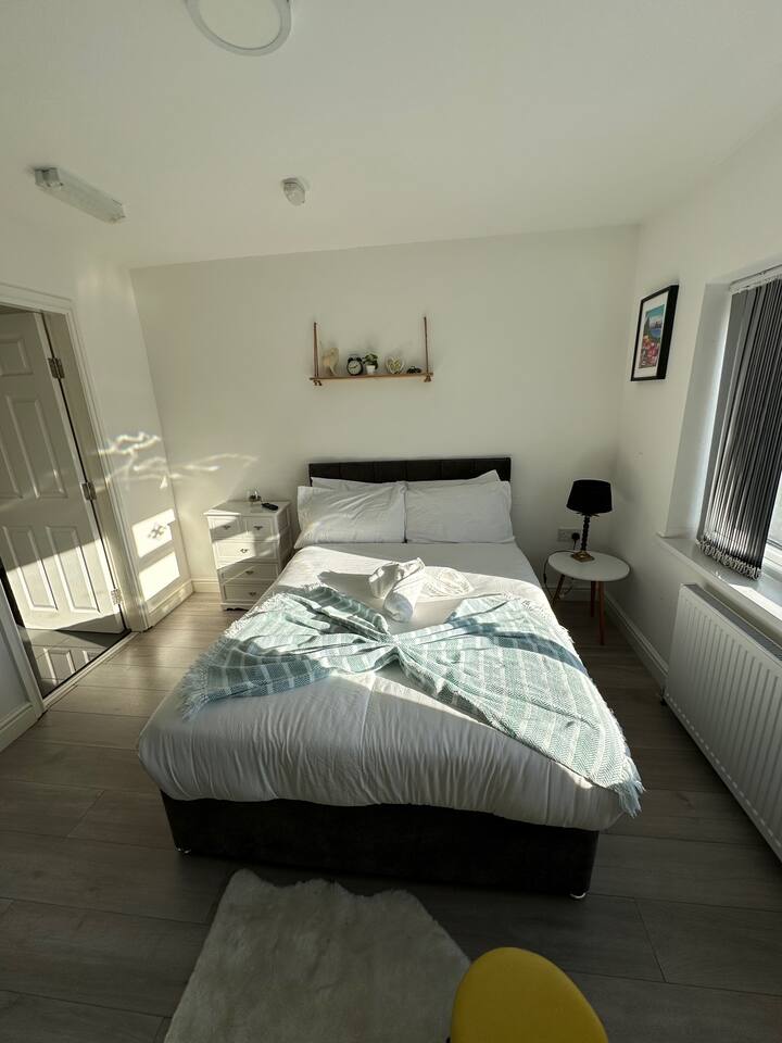 Удобна спалня с двойно легло, закачалки за дрехи, прозорец, носещ слънчева светлина и гледки, и стени, украсени с рамкирани снимки и елегантни щрихи.