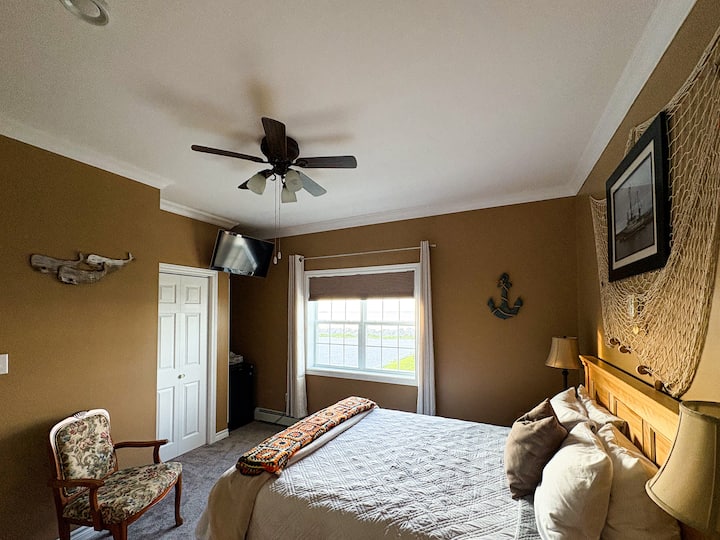 غرفة نوم واسعة بسرير كوين مع مروحة سقف وإضاءة طبيعية ولمسات ساحلية. مصمم للراحة بعد يوم في حديقة غروس مورن الوطنية.