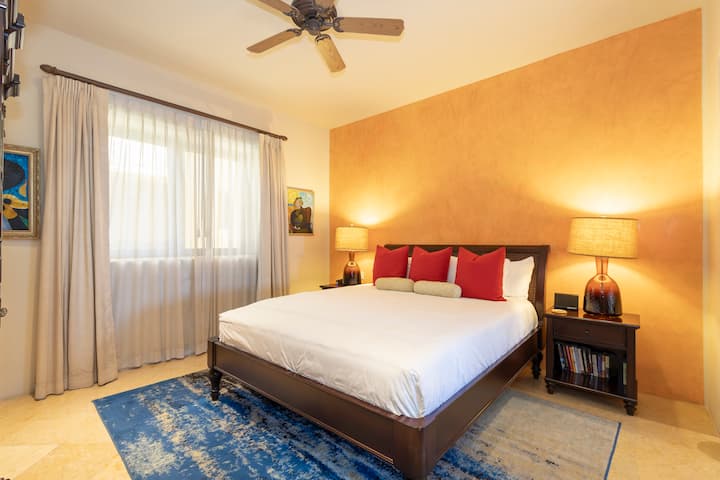 Sink into crisp white linens accented with vibrant red pillows in your serene bedroom retreat. The warm golden accent wall and soft lighting create an inviting ambiance perfect for unwinding after a day of adventure.