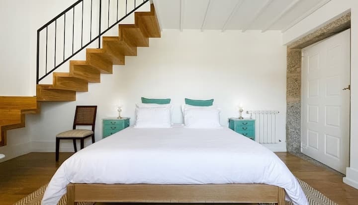 Quarto com cama de casal junto à escada, decorado com bom gosto: acolhedor e luminoso.