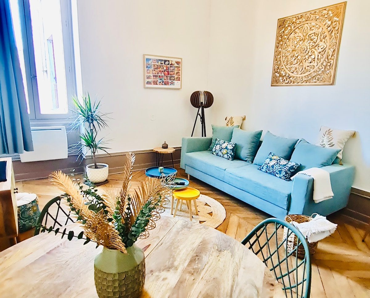 A bright and inviting living space is showcased, featuring a comfortable blue sofa adorned with patterned cushions. A round coffee table occupies the center, surrounded by colorful decor elements. A large potted plant adds a touch of greenery, and a decorative wall piece enhances the ambiance.