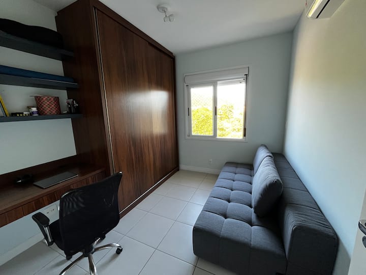 El tercer dormitorio tiene un espacio de oficina en casa con estantes, un banco de trabajo, una silla ergonómica, un armario y un sofá cama.