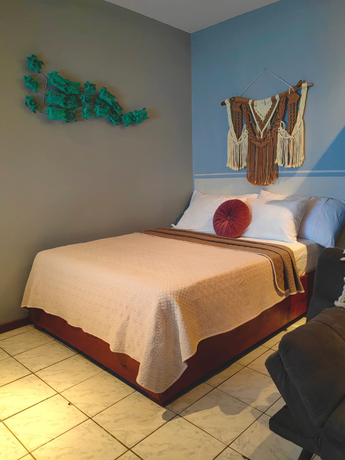 A cozy sleeping area features a spacious bed with a light-colored quilt and an accent pillow. The wall displays a decorative piece made of textured materials, while neutral tones are complemented by a pop of color in the wall art.