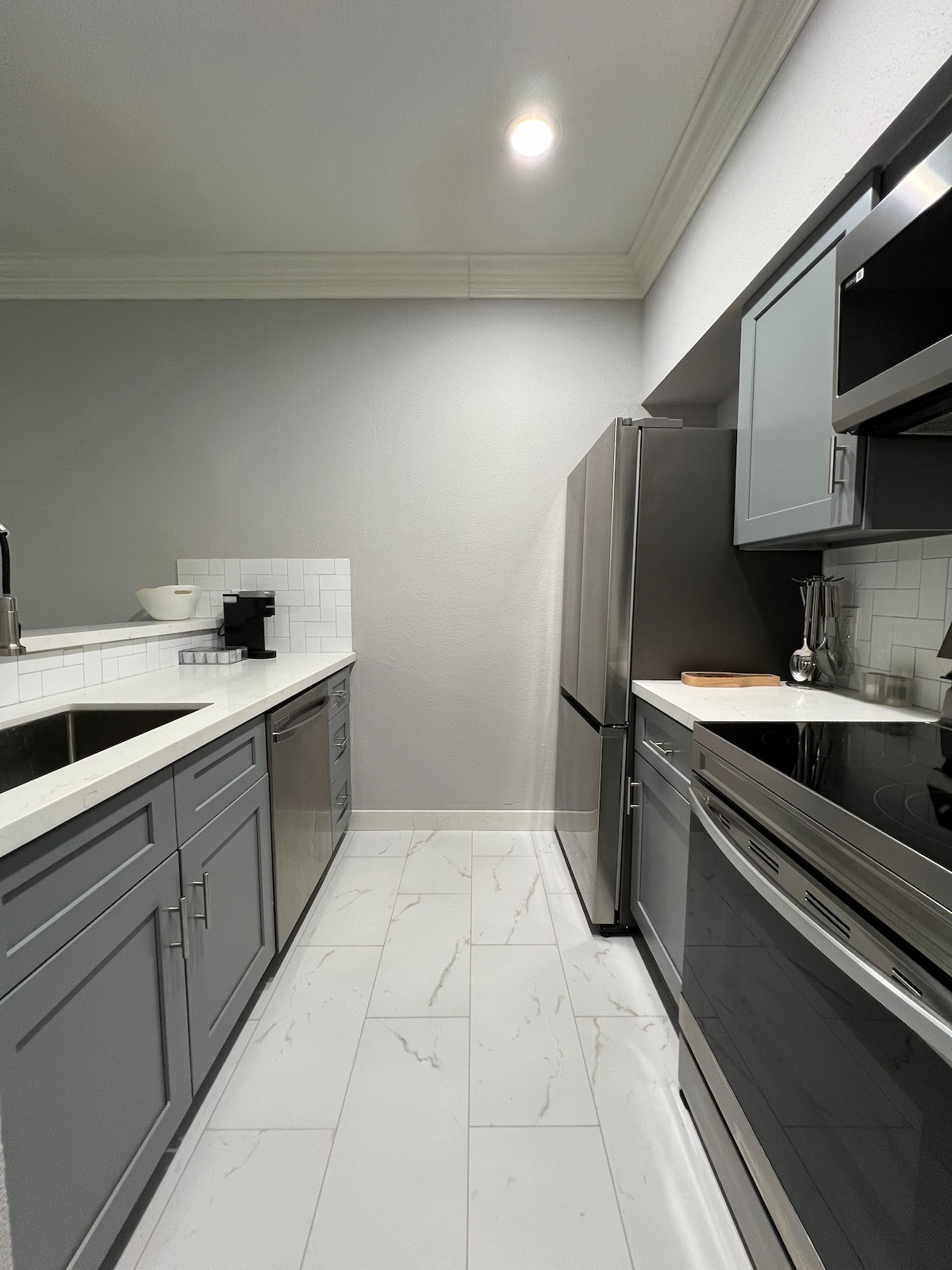 A modern kitchen is equipped with stainless steel appliances including a refrigerator, stove, and dishwasher. Gray cabinetry provides ample storage, and a white countertop contrasts with the light gray walls. A coffee maker is visible on the counter, adding functionality.