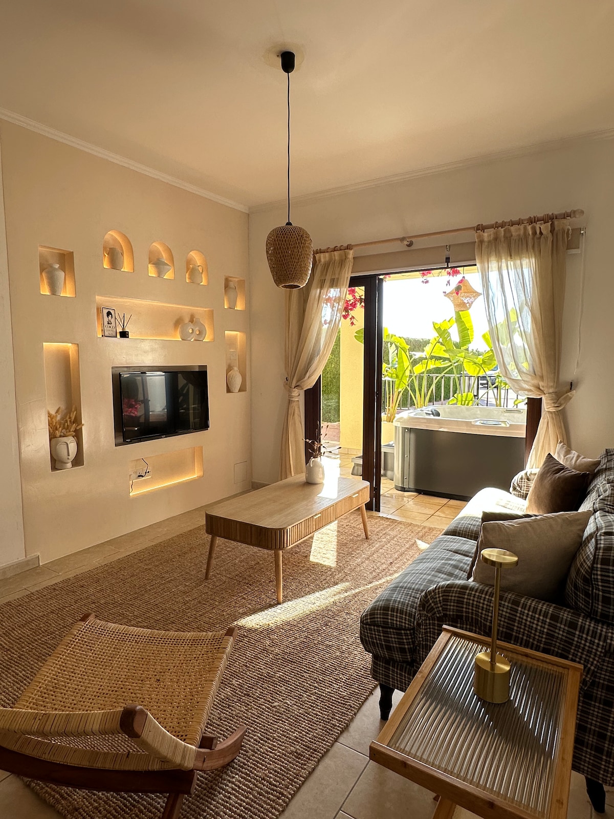 A bright living area features a comfortable sofa next to a stylish coffee table. Natural light enters through the glass doors, leading to a small outdoor space. Decorative wall niches and soft furnishings add character, while a modern pendant light completes the inviting atmosphere.