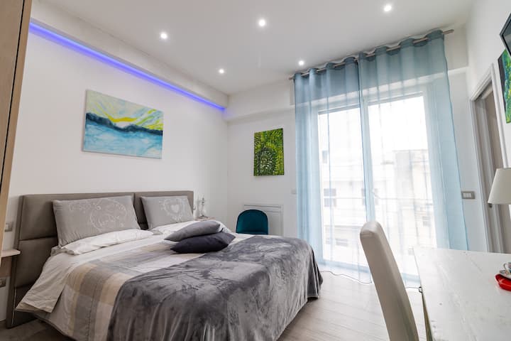 Habitación doble luminosa con iluminación de techo LED azul, cabecera gris y mesitas de noche suspendidas. Arte marítimo y decoración moderna.