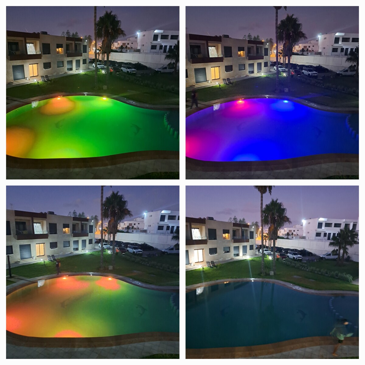 The image showcases a tranquil swimming pool surrounded by lush greenery, illuminated by soft, colorful lights creating a calming ambiance. The pool area is framed by multiple buildings, with cars visible in the background. Dusk light casts a serene atmosphere over the scene.