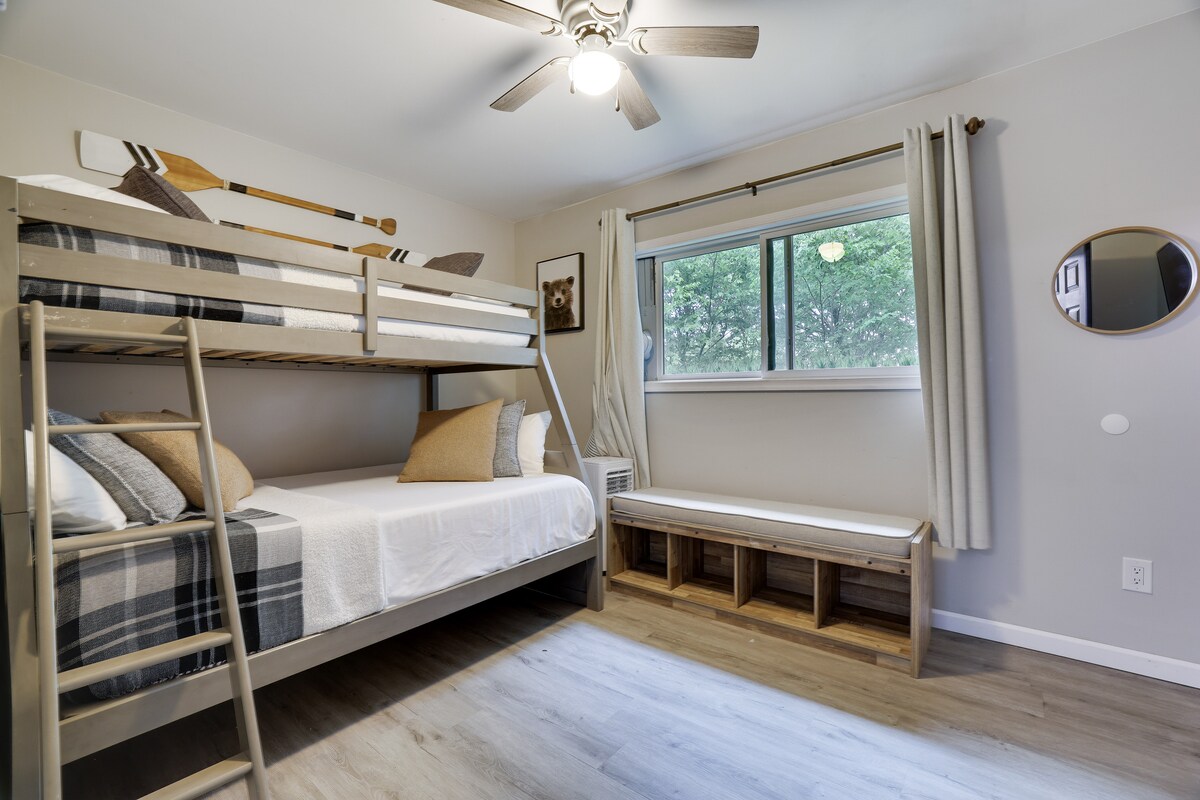 Este cálido dormitorio de madera cuenta con una litera con una cama de tamaño completo debajo y una doble arriba, ideal para hermanos o invitados. Un televisor proporciona entretenimiento y un banco de almacenamiento mantiene el espacio organizado, creando un refugio acogedor. 