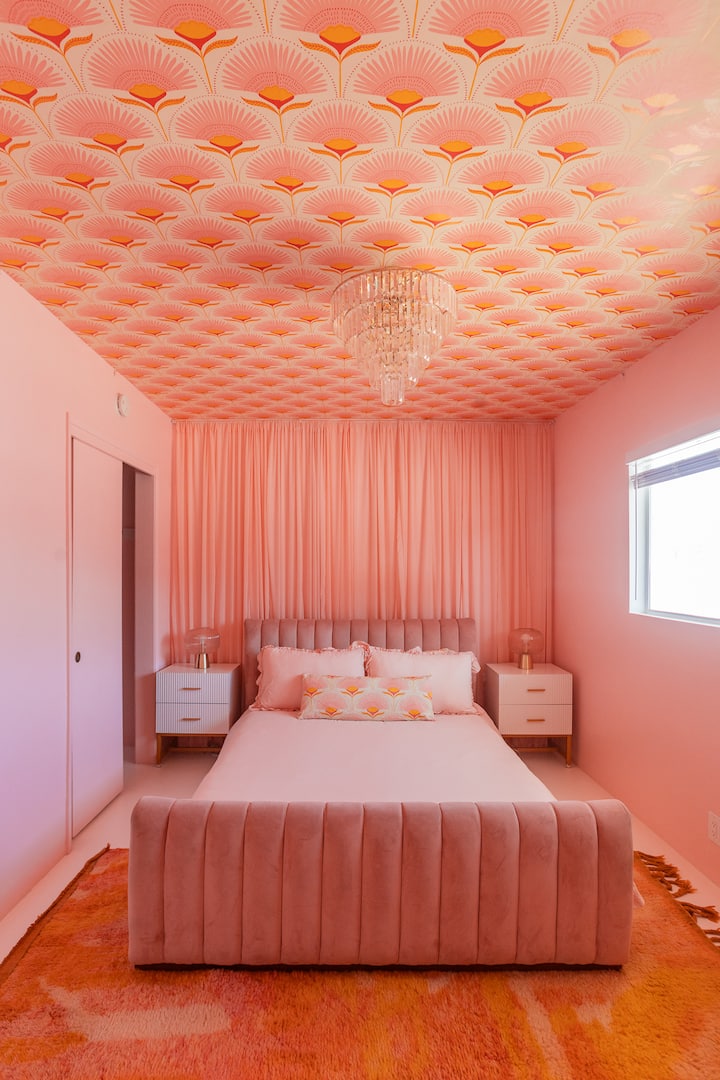 Fully pink bedroom with velvet bed, statement wallpaper ceiling, fabric accent wall, and chandelier. Bold, romantic, and designed for a boutique hotel feel - perfect for photos, girls trips, or a dreamy getaway.