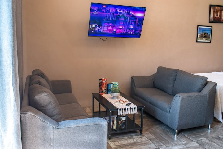 Salon intégré confortable bénéficiant de la lumière naturelle, doté d'un écran de télévision et d'un accès au jardin, avec des jeux de société et une sélection soignée d'ouvrages littéraires à découvrir.