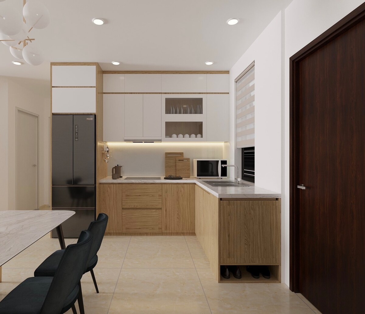 A modern kitchen features sleek cabinetry with a combination of wood and white finishes. Stainless steel appliances include a refrigerator and microwave. A marble countertop extends over the kitchen area, with dishware displayed on shelving above, and a doorway provides access to the adjacent space.
