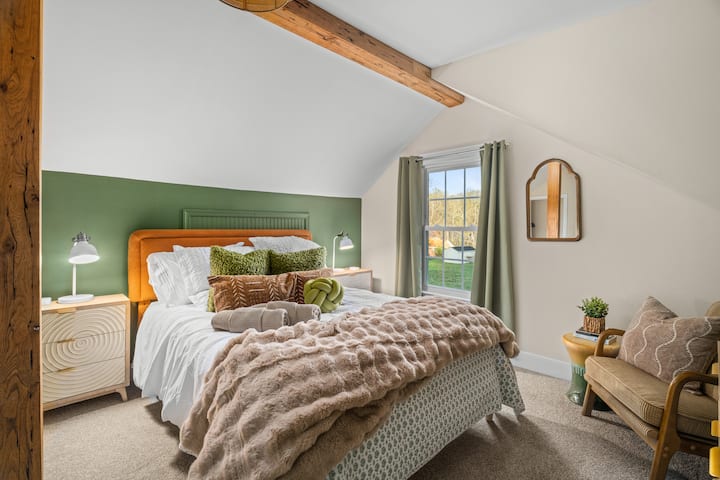 Cozy loft bedroom with exposed beam, green accent wall & sunlight