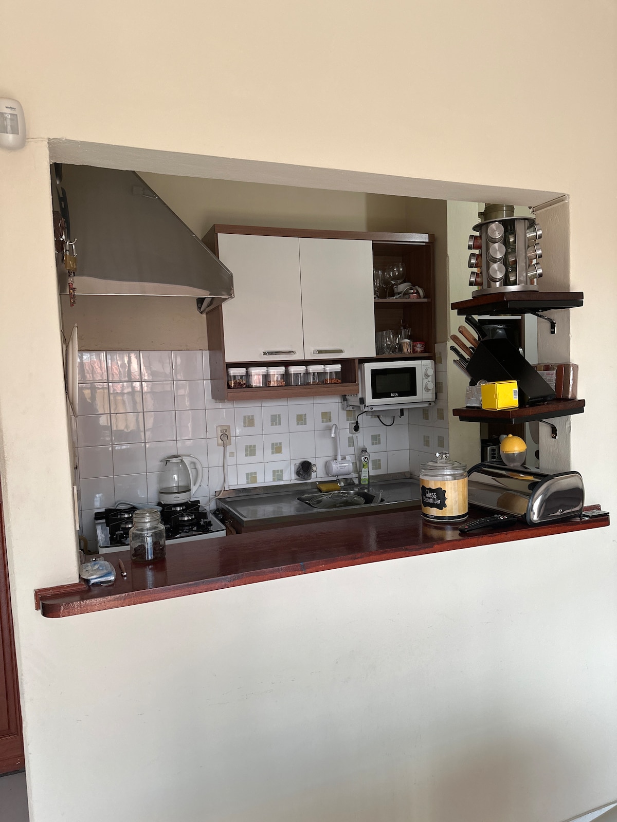 The kitchen area features an open design with modern cabinetry and a range of appliances. A compact countertop is equipped with a stove, microwave, and toaster. Various cooking tools are neatly arranged on a shelf, creating an organized and functional space.