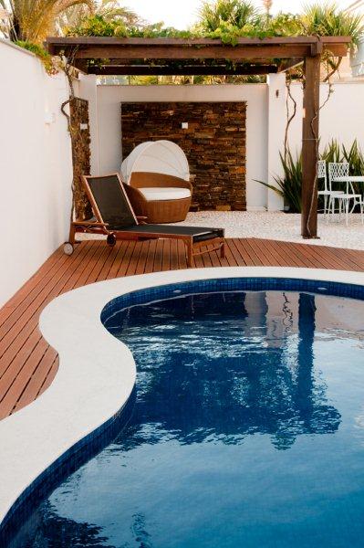 A private outdoor space features a circular swimming pool surrounded by a wooden deck. A lounge chair is positioned beside the pool, alongside a cozy seating area and a shaded structure with a decorative stone wall.