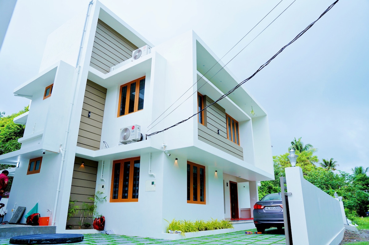 The exterior of the villa showcases a contemporary design with clean lines and a white color palette. Large windows allow natural light to fill the spaces, while the neatly landscaped surroundings feature well-maintained greenery, creating an inviting entrance for guests.