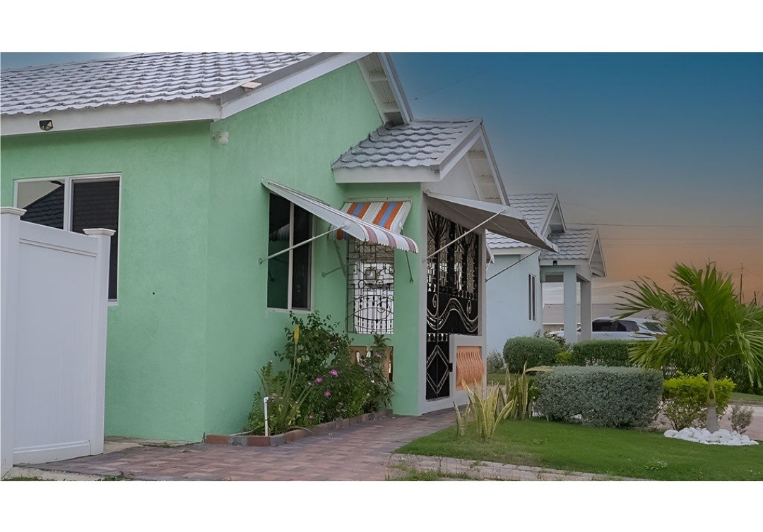 A colorful exterior features a house painted in light green, with a striped awning providing shade over the entrance. Surrounding greenery includes well-manicured bushes and palm plants, creating a refreshing, inviting space. A paved pathway leads to the front door, enhancing the welcoming ambiance.