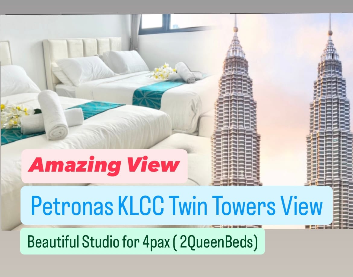 A bright studio space is showcased with two spacious beds dressed in white linens, positioned near large windows that offer a direct view of the Petronas KLCC Twin Towers. Soft towels are neatly arranged on the beds, complementing the modern interior design.