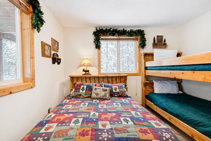 A bedroom featuring a queen bed and a bunk bed, offering flexible sleeping space for families or groups. The room includes soft lighting and a window with woodland views, creating a cozy cabin feel without overpromising.