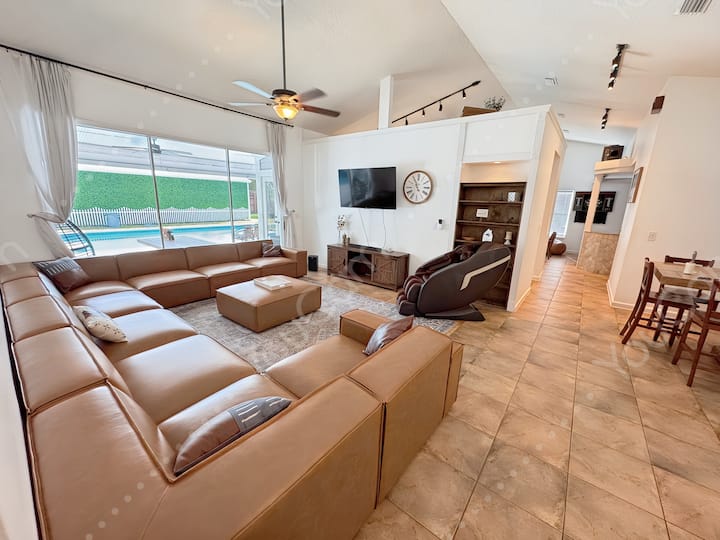 Living area #1 offers a over-sized 9 seater couch, power massage chair, side table with phone charger, and wall-mounted TV with soundbar.