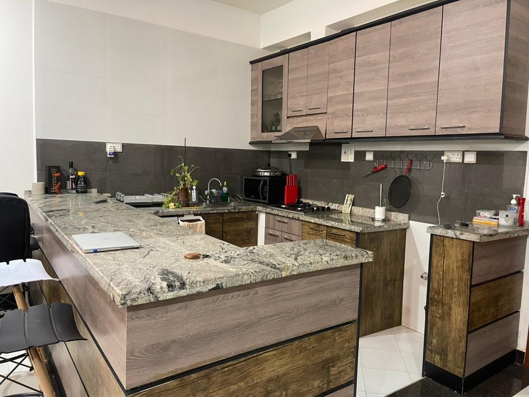 A modern kitchen features sleek cabinetry with a combination of light and dark finishes. A spacious countertop made of granite provides ample room for meal preparation. Kitchen appliances, including a microwave and stovetop, are positioned for convenience, surrounded by organized utensils and small plants.