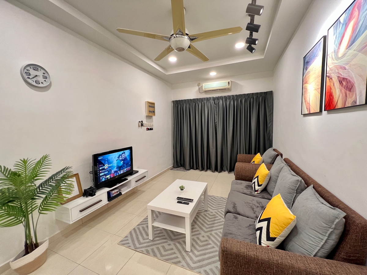 A cozy living area is highlighted by a comfortable sofa adorned with yellow and grey cushions. A white coffee table sits on a geometric-patterned rug, while a television is positioned on a wall-mounted unit. Natural light filters through dark curtains, and a ceiling fan provides airflow.