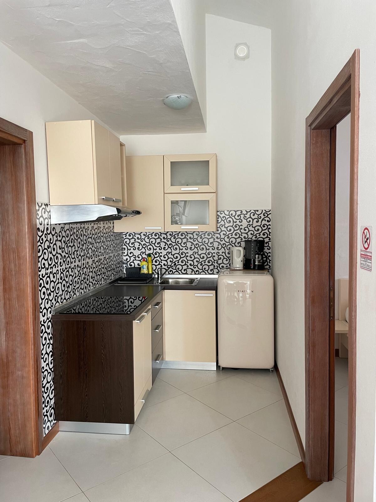 A modern kitchen area showcases sleek cabinetry in two-toned finishes. The countertop is equipped with a stove and a sink, while a retro-style refrigerator is positioned nearby. A patterned backsplash complements the design, enhancing the functional layout of the kitchen.